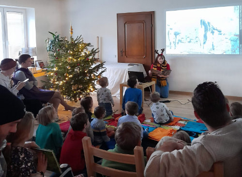 Irina liest das Bilderbuchkino Lieselotte Weihnachtskuh vor, während viele Kinder davor sitzen und aufmerksam zuhören